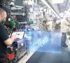 Ein Bosch-Mitarbeiter mit einem Tablet steht in einer Produktionshalle und blickt auf die Illustration einer 3D-Grafik.