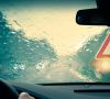 Ein Autofahrer sitzt bei schlechten Wetterverhältnissen hinteerm Steuer und sieht nur noch den Regen auf der Windschutzscheibe und ein warnendes Verkehrsschild.