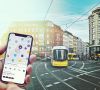 Smartphone mit Mobilitäts-App vor Tram in der Stadt.