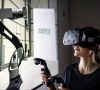Eine Frau mit VR-Brille blickt auf einen Cobot.